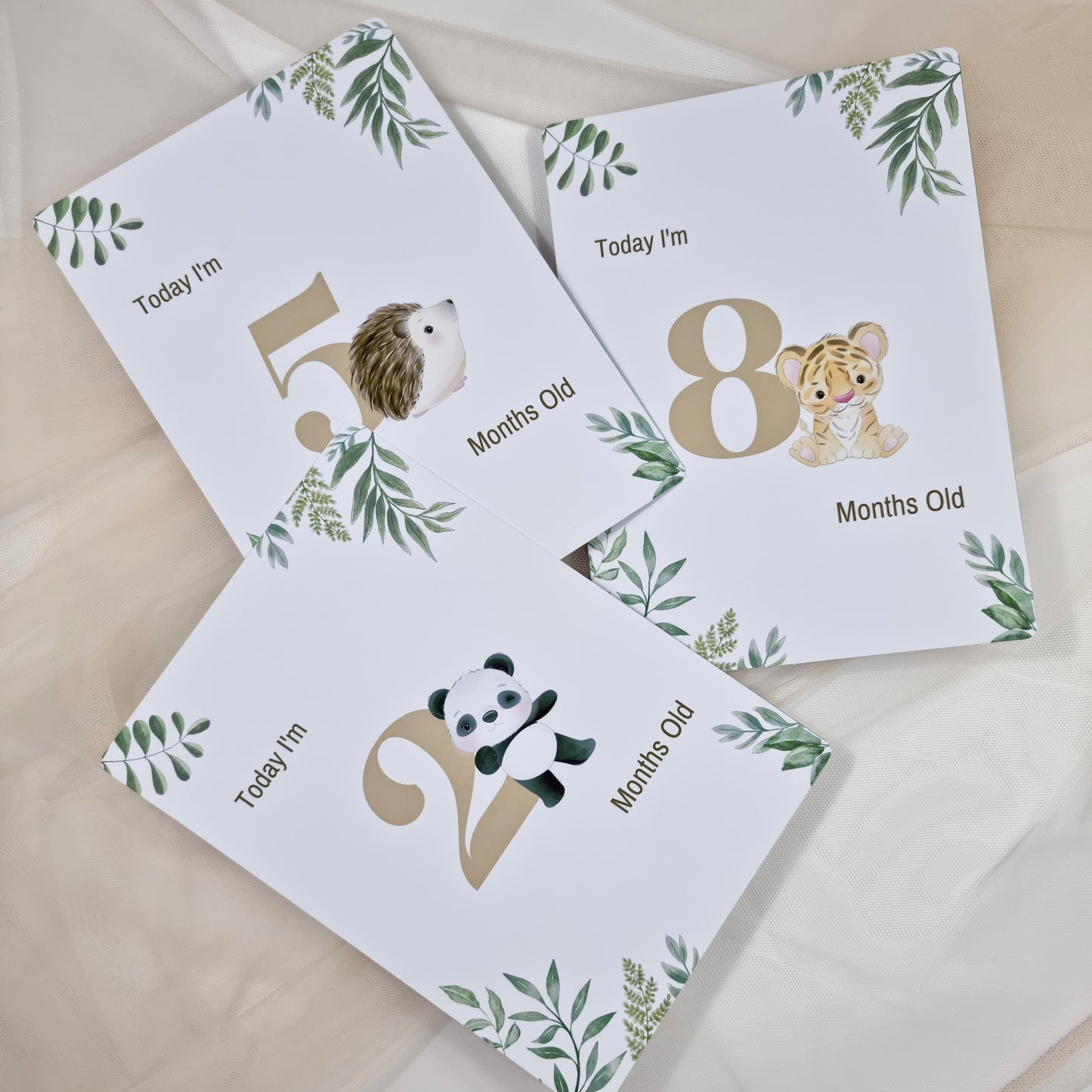 Three milestone cards for 5, 8, and 10 months old with animal illustrations on a beige background.