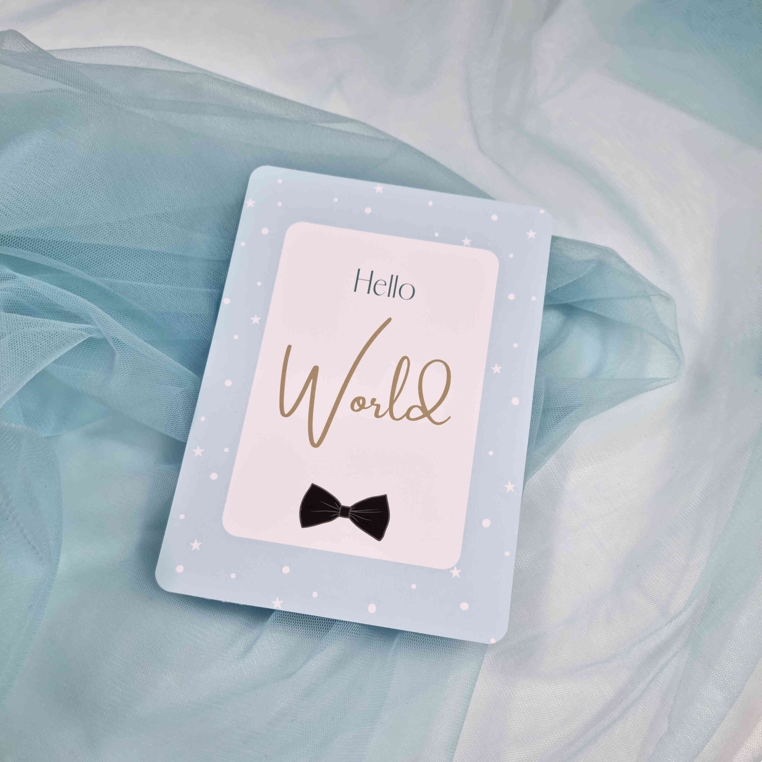 Card with 'Hello World' and a bow tie on a light blue fabric background