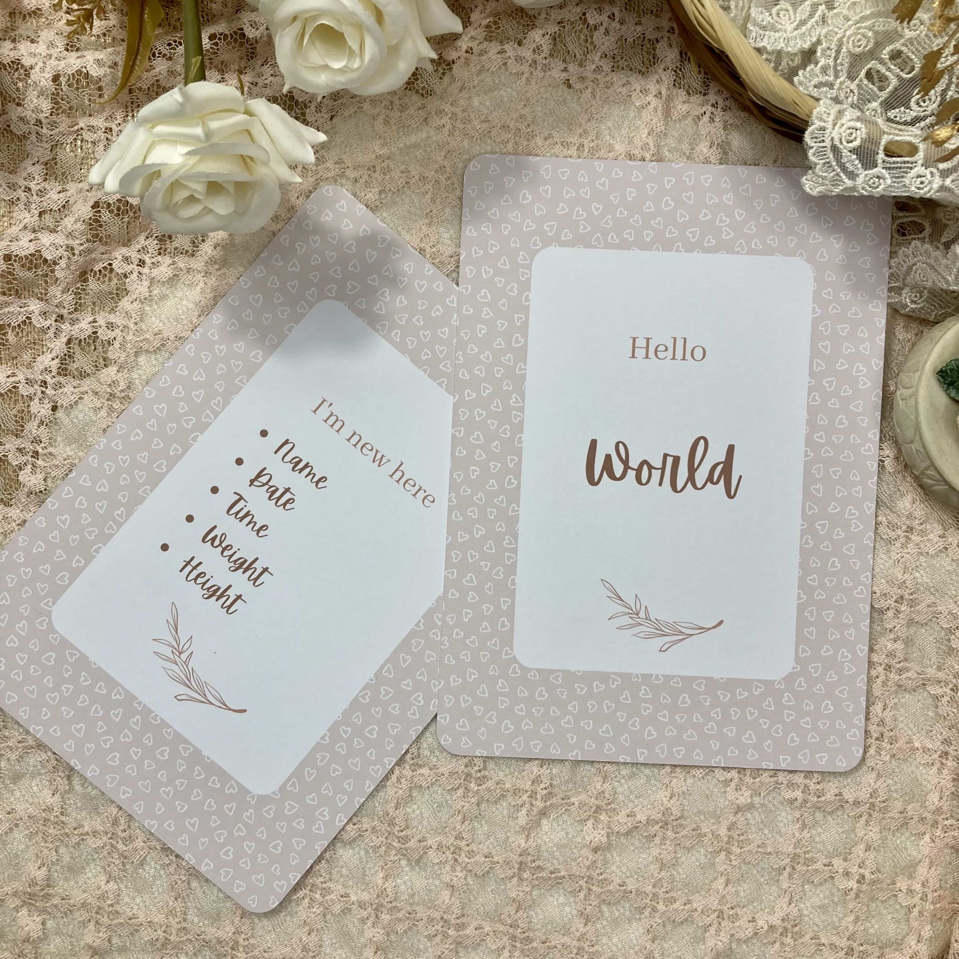 Two milestone cards on a textured surface with white roses and decorative elements.