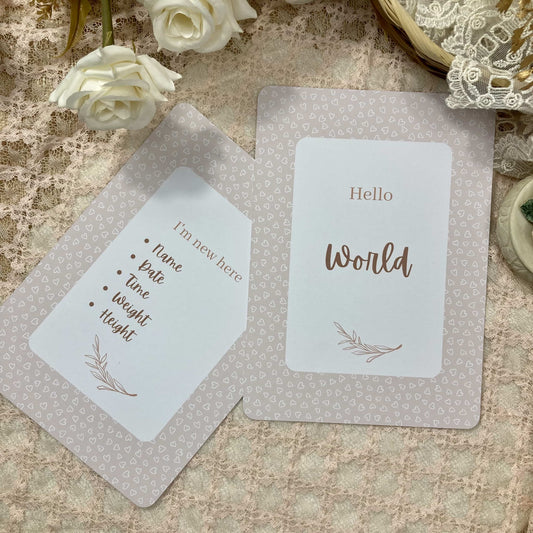 Two milestone cards on a textured surface with white roses and decorative elements.